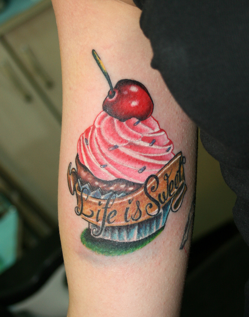 Life Is Sweet Banner With Cake Tattoo On Bicep